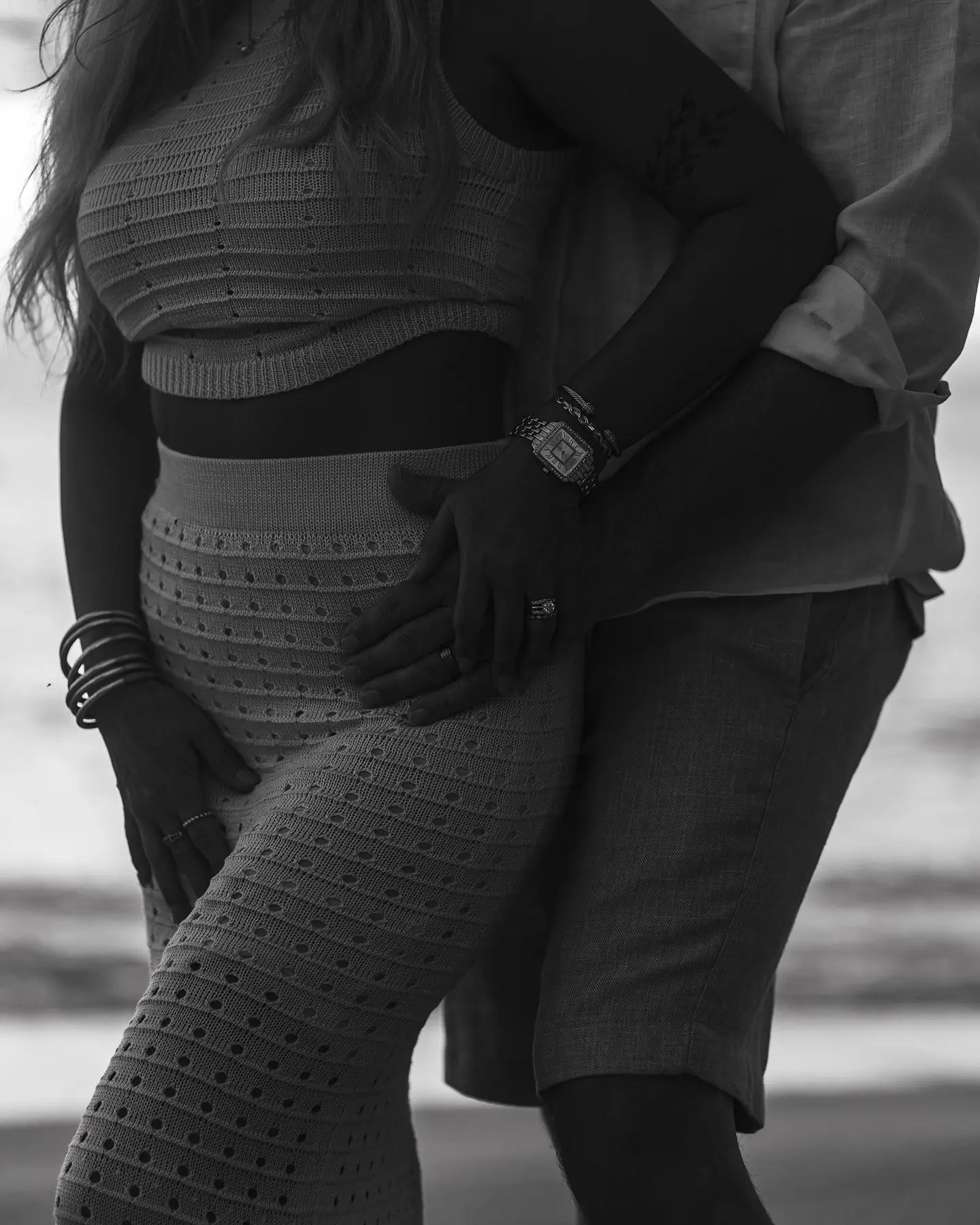 A couple embracing on the beach, with the woman wearing a fitted crop top and a long skirt. The image is in black and white, highlighting their close connection.